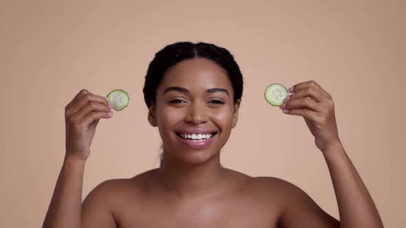 Young Pretty African American Woman Taking Away Fresh Cucumber Slices From Eyes and Smiling to