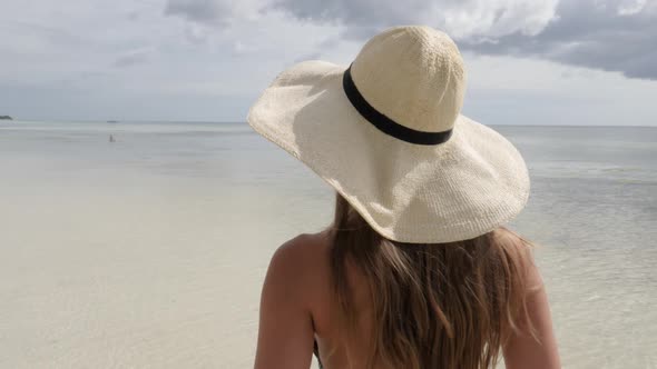 Close up shot from behind a young tanned woman with long brown hair and hat looking at beautiful bea