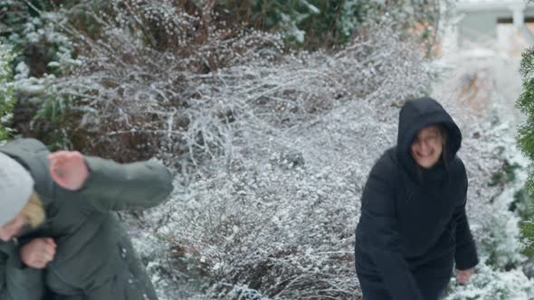 Excited Beautiful Young Woman Playing Snowball Fight with Friend on Cold Winter Day Outdoors