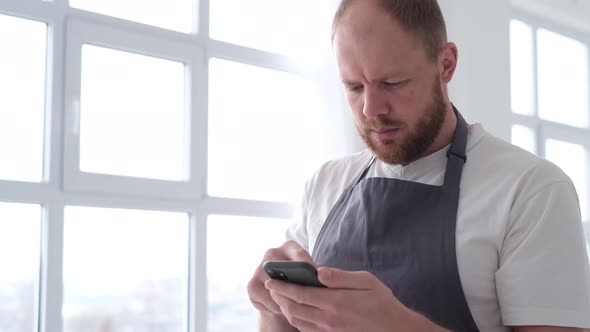 A Professional Artist in the Studio He Holds a Smartphone and Browses Modern Paintings