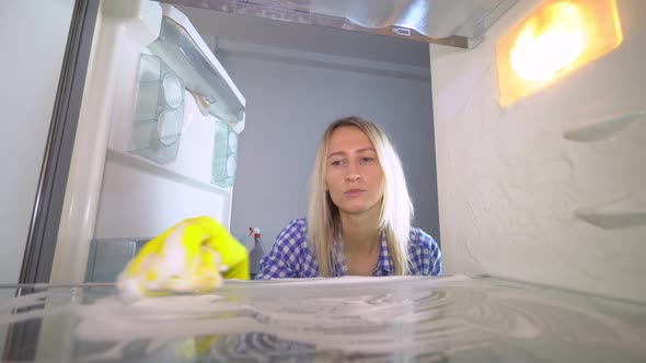 A disgruntled and irritated woman washes and cleans inside the refrigerator