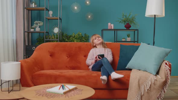 Little Elementary School Kid Girl Using Mobile Phone Technology Device Sitting on Sofa Alone at Home