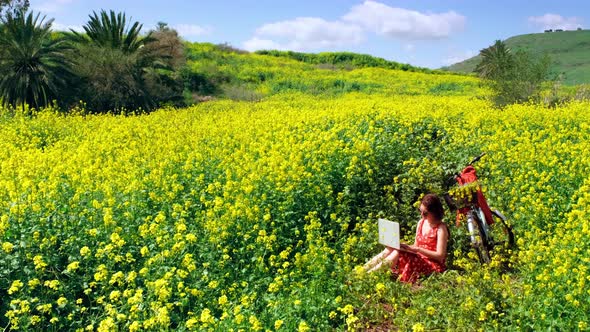 Freelancer Girl Works Behind a Laptop in a Spring Flower Field