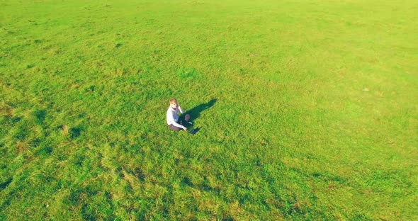 Low Orbital Flight Around Man on Green Grass with Notebook Pad at Yellow Rural Field