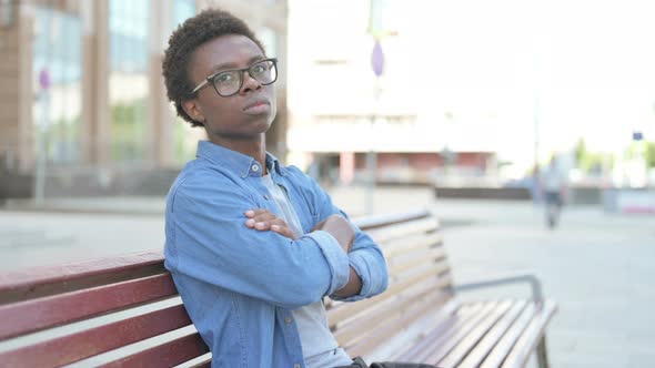 Young African Man Looking at Camera While Sitting on Bench