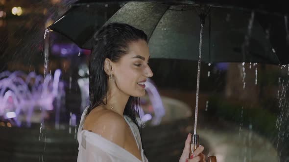 Pretty Woman Posing with Umbrella Under Fountain Waterfall in Evening