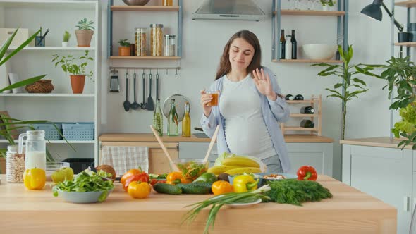 Happy Pregnant Woman Drinks Vegetable Fruit Juice in the Kitchen