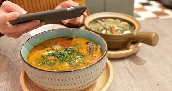 Woman Using Cellphone and Taking Photo on The Soup Bowl