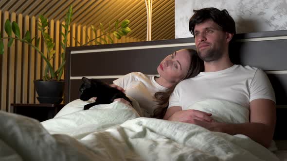 Couple Watching TV at Night at Home Lying on the Bed