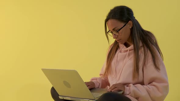 Mixed-race Young Lady Working on the Computer on Yellow Background