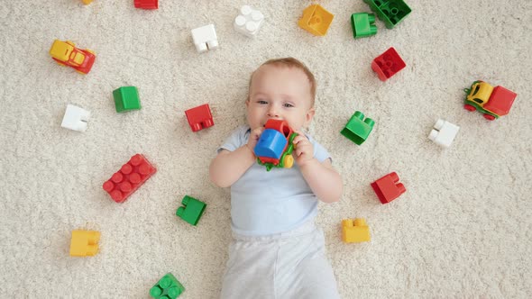 Portrait of Smiling Baby Boy Surrounded with Lots of Toys Lying on Carpet in Playroom