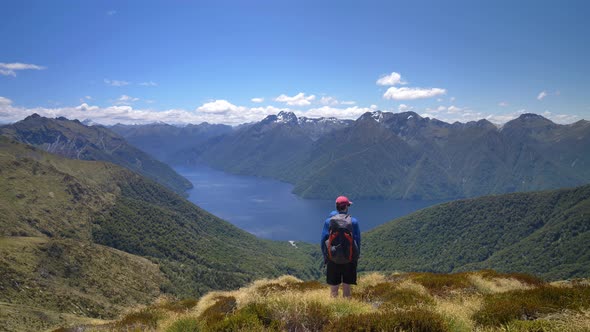 Static, hiker overlooks landscape of lake surrounded by mountains, Kepler Track New Zealand