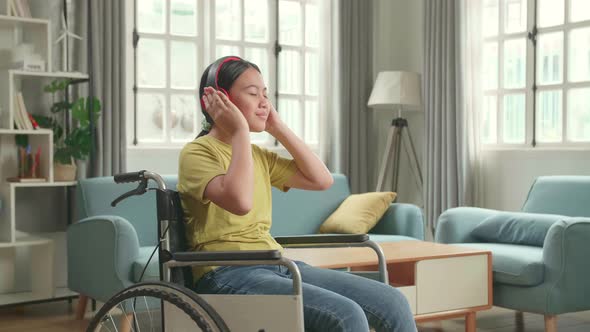 Asian Kid Girl Sitting In A Wheelchair Listening To Music With Headphones And Dancing In Living Room