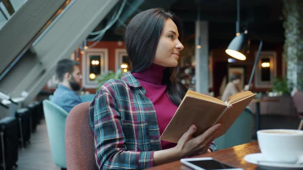 Intelligent Young Woman Reading Book Enjoying Literature Sitting at Table in Cafe