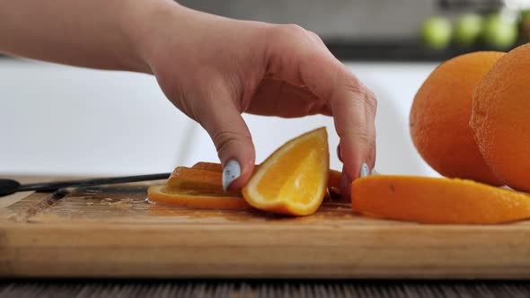 Women's Hands with a Knife Cutting Orange on the Cutting Board