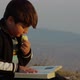 Boy Reads a Book and Eats an Apple in the Rays of the Sunset on the Background of Mountains - VideoHive Item for Sale