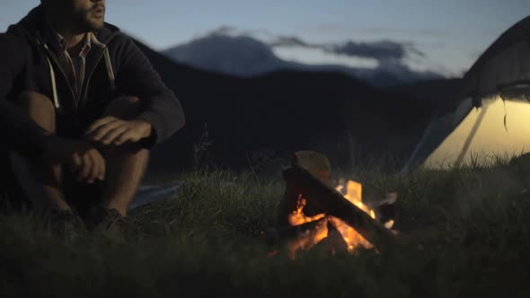 Young Man Warming with Camp Fire in Nature Mountain Outdoor Camping Scene at Night Dolly