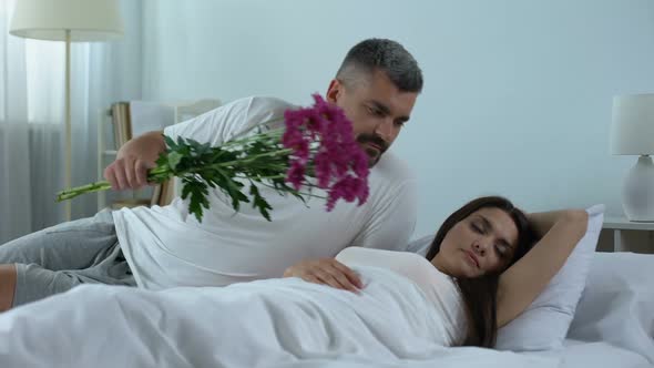 Attentive Man Waking Up Wife With Bouquet of Flowers, Romantic Relationship Care