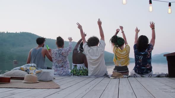 Friends Sitting on Pier and Waving Arms at Lake Party