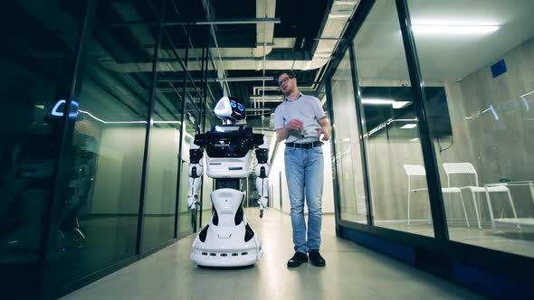 Male Specialist is Showing a Business Hall to a Robot