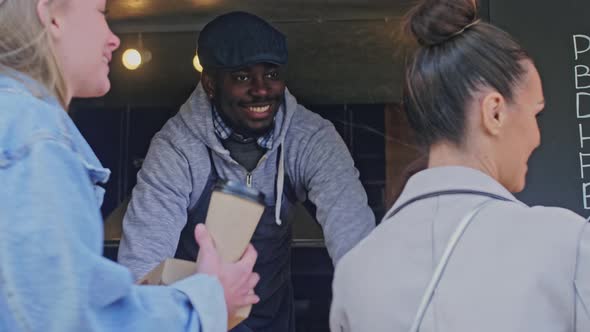 Smiling seller holding out order to clients through the window food truck