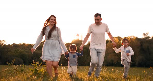 Happy Family Their Man with Two Children Walking on the Field at Sunset in the Sunset Light in the