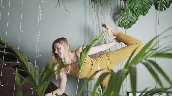 Young Woman Does Yoga Near Wooden Stairs Behind Potplant