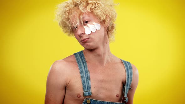 Androgynous LGBT Man Hitting Camera with Flowers Posing at Yellow Background