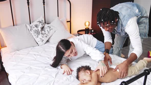 Multiracial Parents Have Fun with Their Toddler Laying Down on Bed Tickling Him and Making Him Laugh