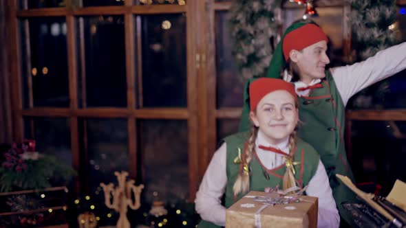 Cheerful elves in festive costumes imitate flying indoors. Happy man and woman in elf costumes