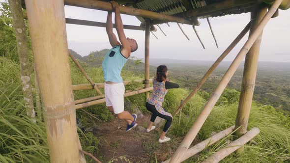 Sport Couple Training Outdoor on Green Hill and Mountain Landscape. Sport Man Pulling Up