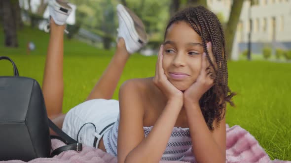 Portrait of Beautiful Happy Girl Lying on Sunny Meadow and Smiling. Positive African American Child