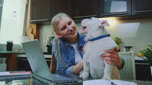 Blonde Girl Petting Bulldog and Speaking with It in the Kitchen at Home