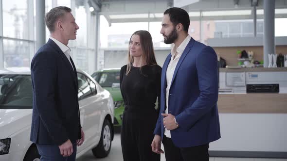 Successful Young Multiracial Couple Choosing Vehicle in Car Dealership. Handsome Middle Eastern Man