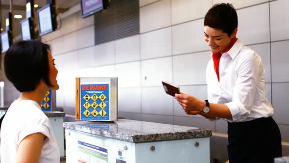 Female airport staff checking passport and interacting with woman at check-in desk