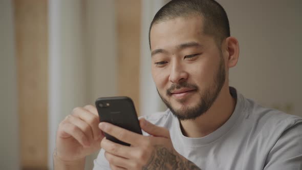 Young Adult Asian Man Browsing on His Smart Phone with Not Bad Facial Expression Indoors