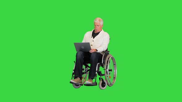 Disabled Old Man in Wheelchair Typing on Laptop on a Green Screen Chroma Key
