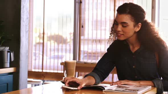 Woman using mobile phone while reading magazine in caf������������