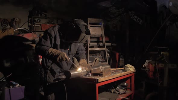 Man fabricating stainless steel pipe shielded metal arc welding in workshop. WIDE SHOT
