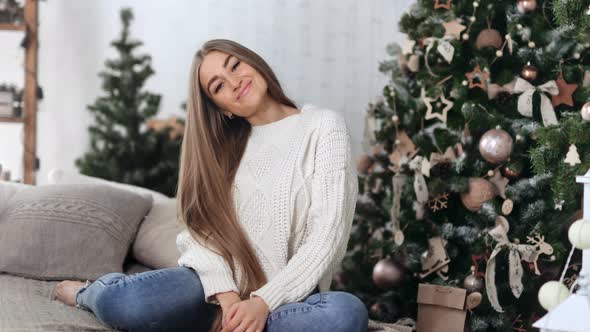 Smiling Domestic Woman Posing on Comfortable Couch with Christmas Tree