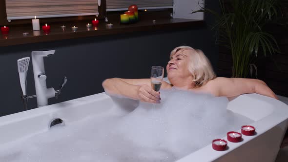 Elderly Senior Woman Lying in Warm Bath with Bubbles, Enjoying Relaxation, Drinking Champagne