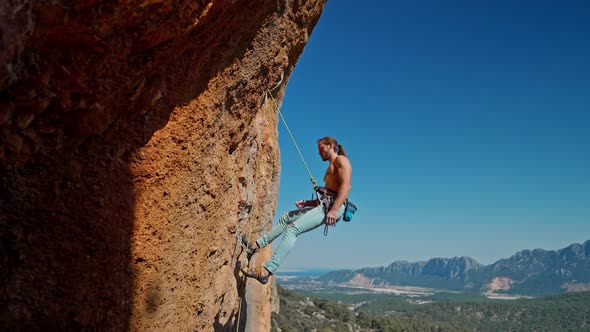 Side View of Strong Handsome Man Rock Climber Descends From Vertical Cliff on Top Rope