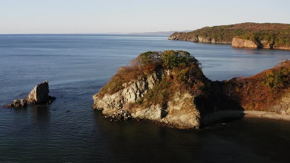 Picturesque Rocky Promontory Covered with Vegetation and Island in the Sea