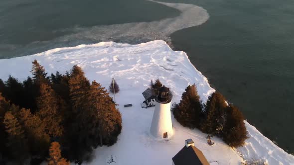 Old Presque Isle Lighthouse in Michigan during the winter with a sunset.