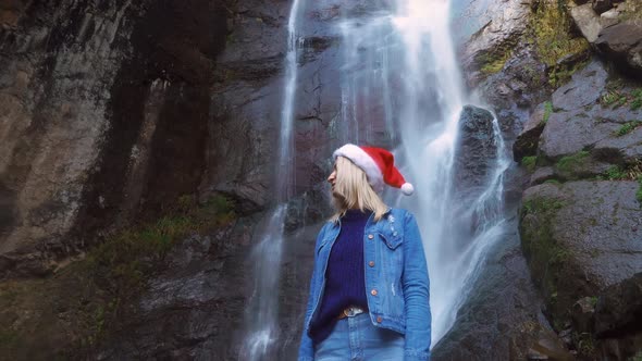 girl in Santa Claus hat stands on waterfall on Christmas Day. Enjoying nature