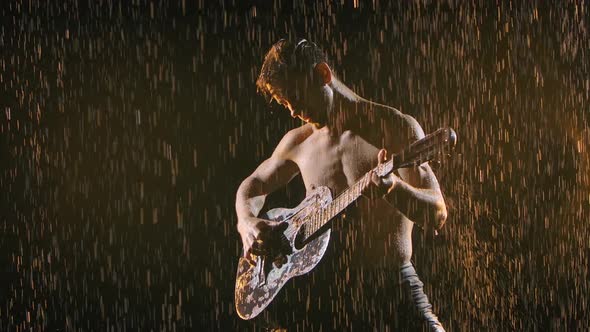 A Wet Man with a Naked Torso Moves Sexually, Plays the Guitar and Sings. Silhouette on a Black