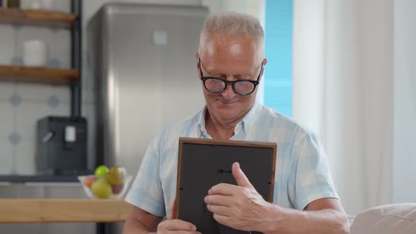 Portrait of Senior Man Looking at Photo Frame at Home