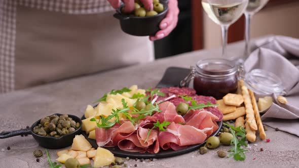 Meat and Cheese Plater at Domestic Kitchen Woman Puts Olives to Serving Board with Sausages Cheese