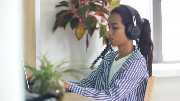 Young Freelancer Woman Working at Home, with a Headphone Typing on a Laptop