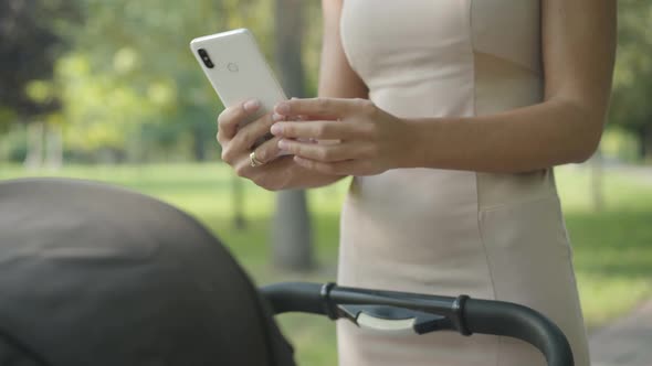 Unrecognizable Young Slim Woman Taking Photos of Infant in Baby Carriage in Summer Park. Young